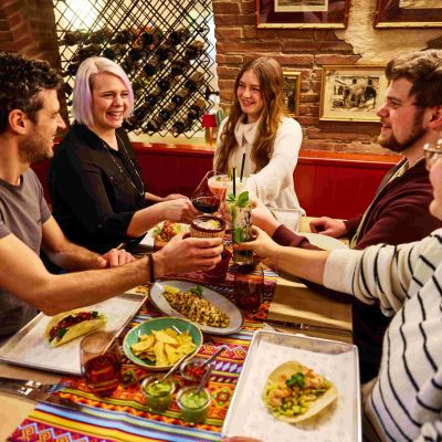 Fünf Gäste sitzen im Restaurant Don Quichotte im Erlebnishotel "El Andaluz" des Europa-Park und stoßen mit ihren Gläsern an.