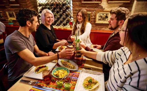 Five guests are sitting in the Don Quichotte restaurant at Europa-Park's El Andaluz themed hotel, clinking their glasses together.