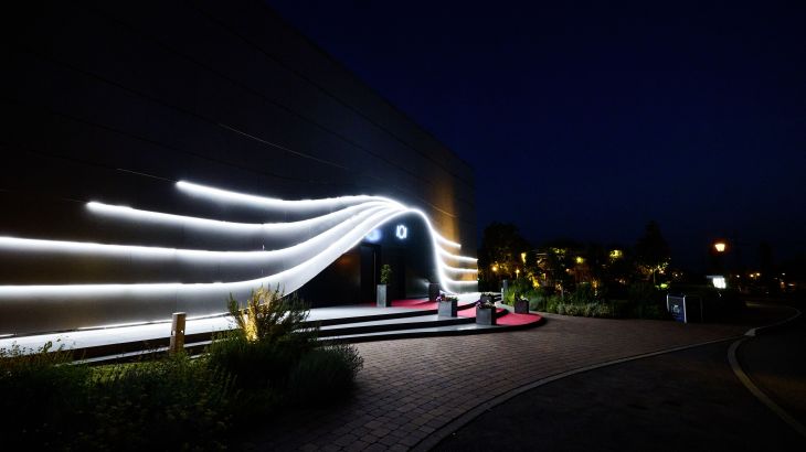 Das Eatrenalin Gebäude bei Nacht mit futuristisch beleuchtetem Eingang und geschwungenen Lichtlinien.