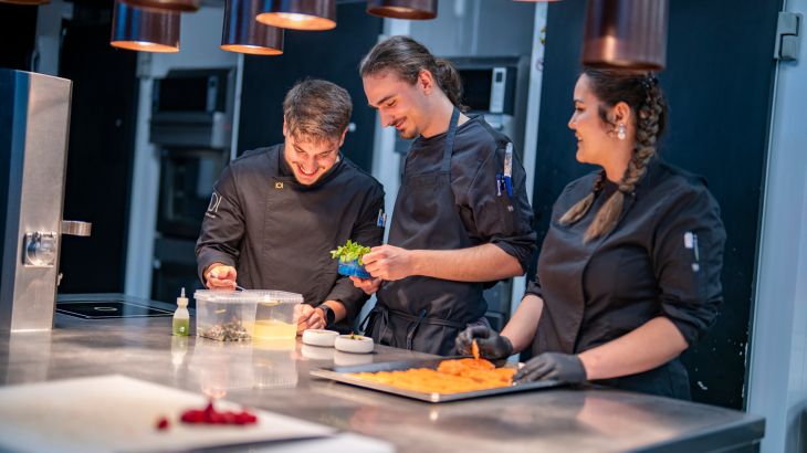 Drei Köche der Fine Dining Experience Eatrenalin bereiten Speisen zum Servieren vor.