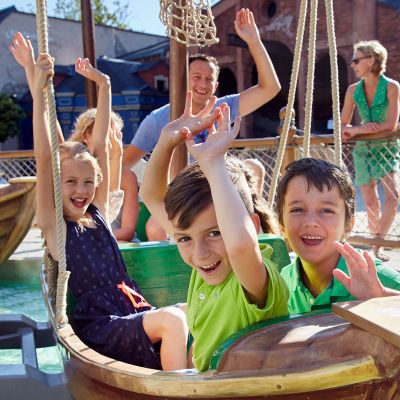 Children sitting in one of the boats on the Sheep Rock carousel ride, with their parents standing at the edge.