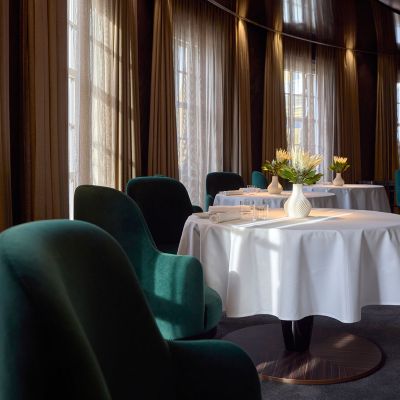 Innenansicht des Restaurants Ammolite – House of Light im Erlebnishotel "Bell Rock". Auf den gedeckten Tischen steht jeweils eine weiße Vase mit Blumen. Die Atmosphäre wirkt sehr modern und edel.