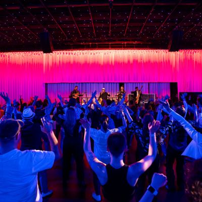 Party guests at the event location The Studio at Europa-Park clap along to live music. A band is performing on stage.
